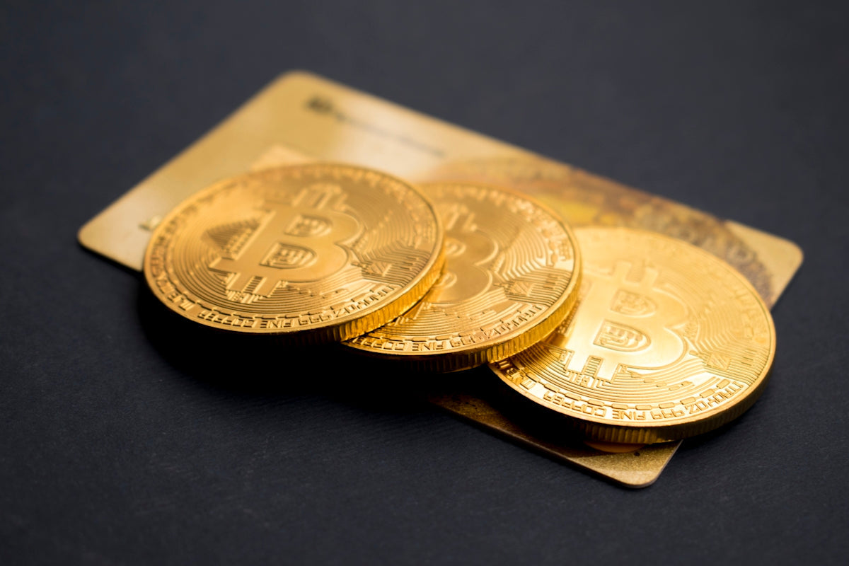 Tri zlatni bitcoin kovanice pored kreditne kartice na crnoj pozadini.