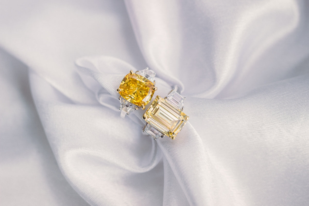 Two dazzling rings rest on a silky white cloth.