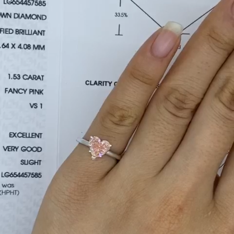 Hand wearing a delicate pink heart-shaped diamond ring, alongside a detailed report sheet.