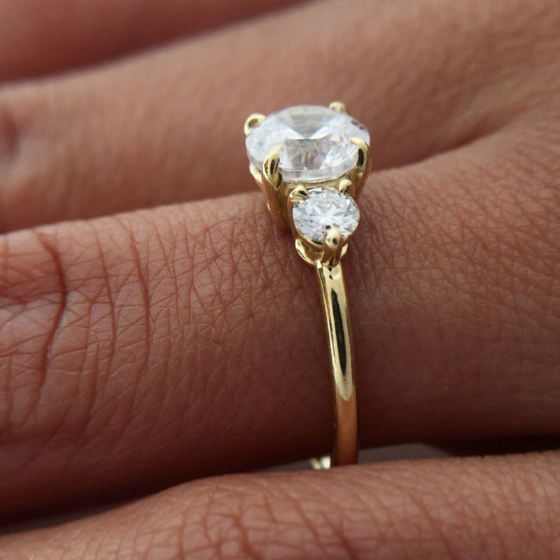 Close-up of a gold engagement ring featuring a large and small diamond on a hand.