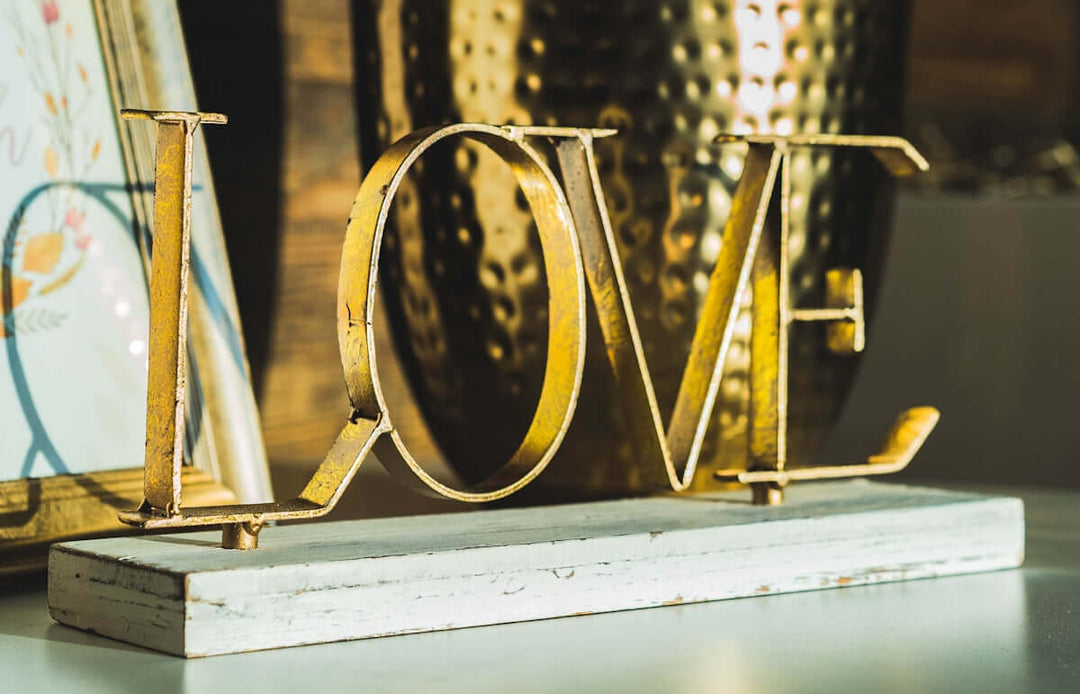 Goud 'liefde' metalen decoratie op een houten basis, omgeven door elegante huisdecoratieven.