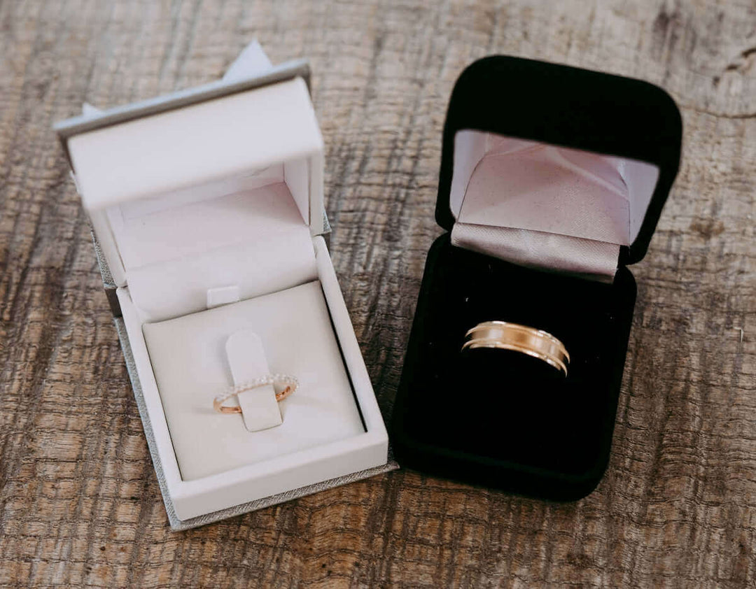 Elegante diamanten ring in witte doos en gouden trouwring in zwarte doos op rustiek houten oppervlak.