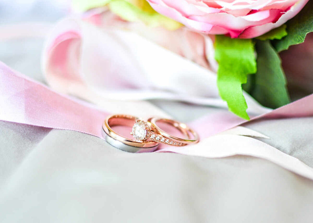 Elegante trouwringen geplaatst op zachte satijnen linten in de buurt van een boeket pastelkleurige bloemen.