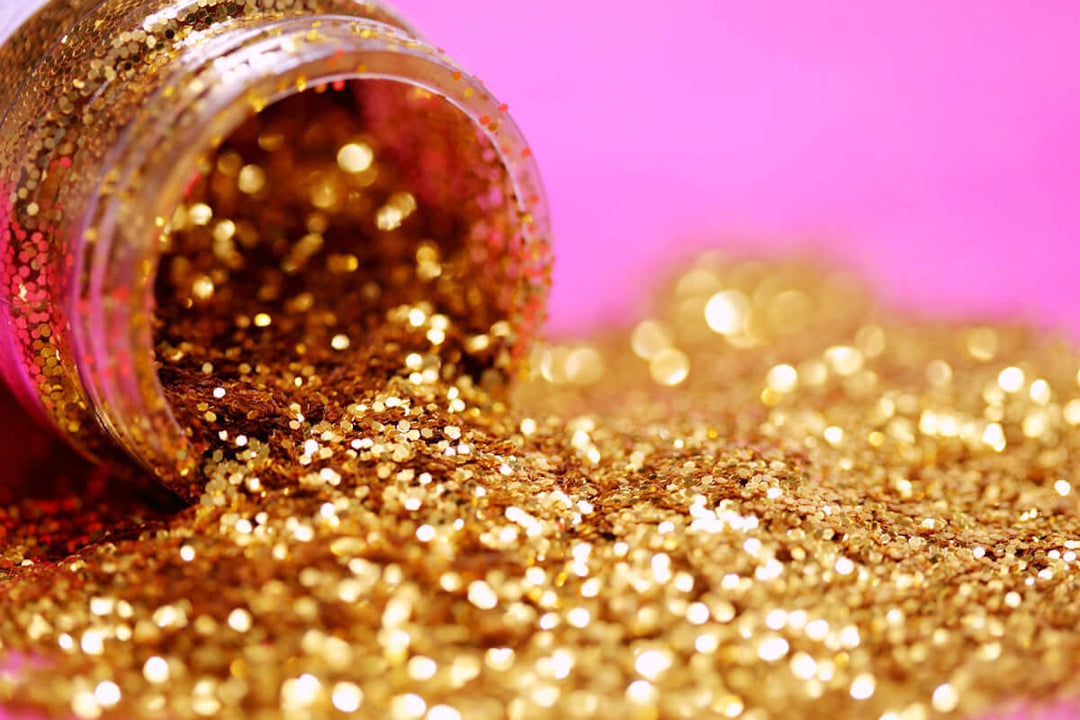 Een pot die gouden glitter morste op een levendige roze achtergrond, perfect voor kunst- en handwerkprojecten.