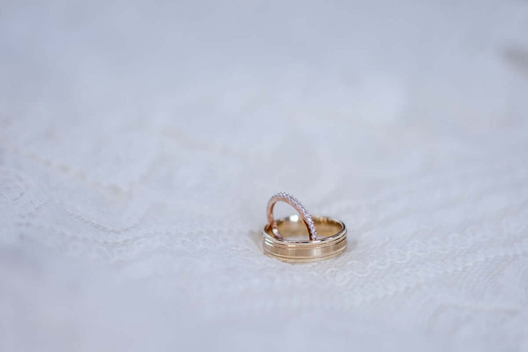 Elegante ovale pavé diamanten verlovingsring gecombineerd met een klassieke trouwring op delicate kanten achtergrond.