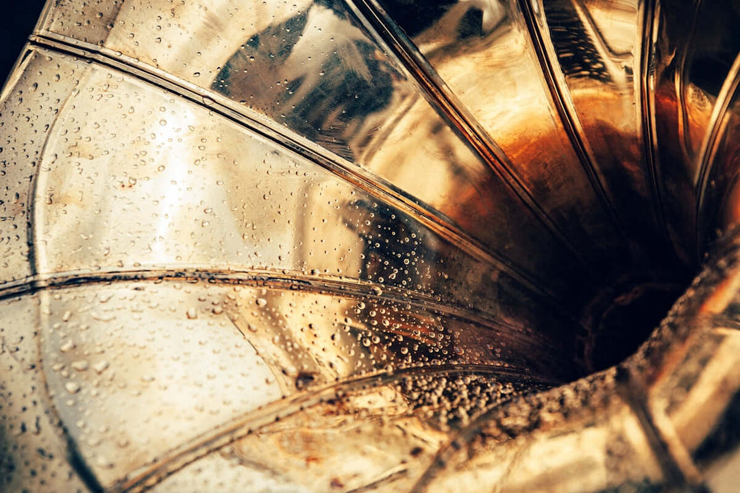 Close-up van een vintage grammofoonhoorn met waterdruppeltjes en een gouden afwerking.