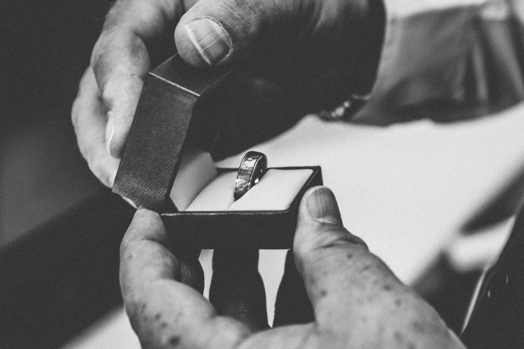 Graustufenfotografie der Person, die silberfarbenen Ring in der geöffneten Schachtel hält