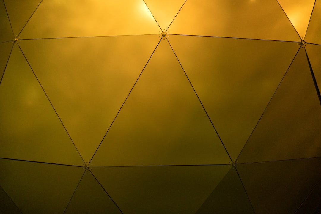Geometrisch patroon van geel getinte driehoekige panelen die licht reflecteren.