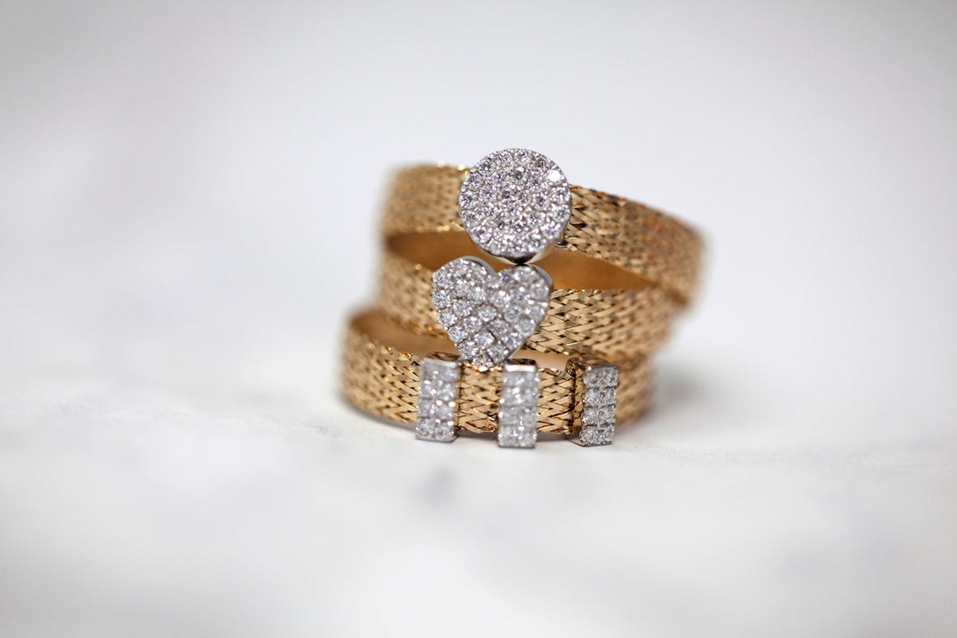 Drie gouden ringen met sprankelende diamantaccenten in hart- en cirkelvormige ontwerpen.