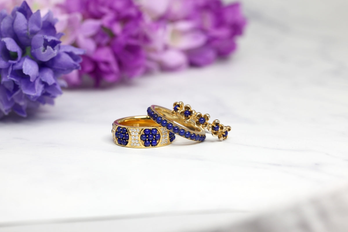 Elegant gold rings adorned with blue stones, set against a backdrop of purple flowers.