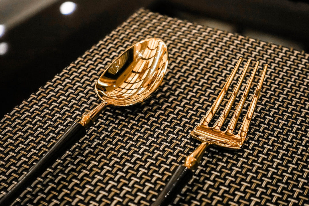 Elegante gouden lepel en vork op een gestructureerde zwarte placemat, perfect voor luxe dineren.