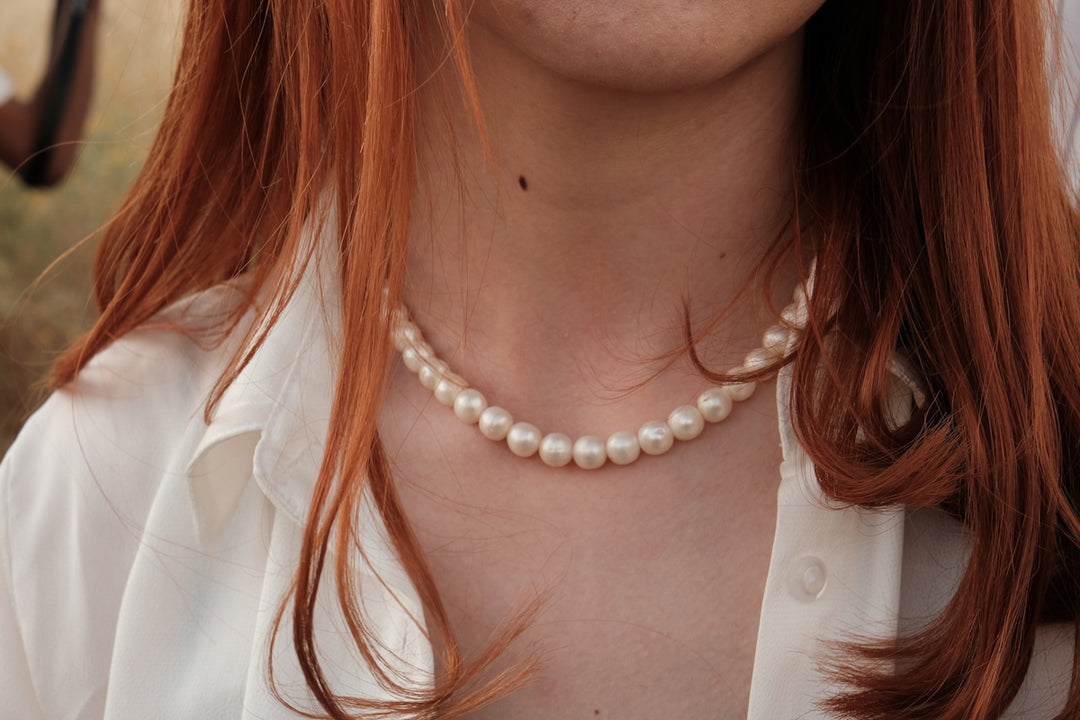 a woman with red hair wearing a pearl necklace